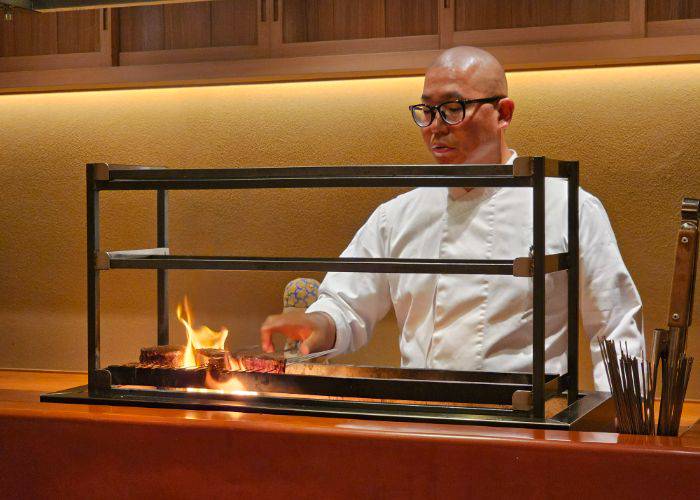 Chef Katayanagi laying wagyu beef above smoldering charcoal.